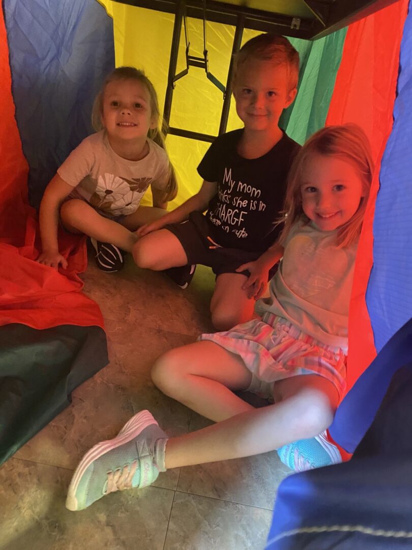 Three kids sitting in a rainbow tent
